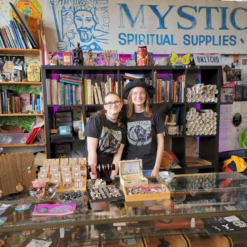 Two witches standing behind the buckland museum gift shop counter.